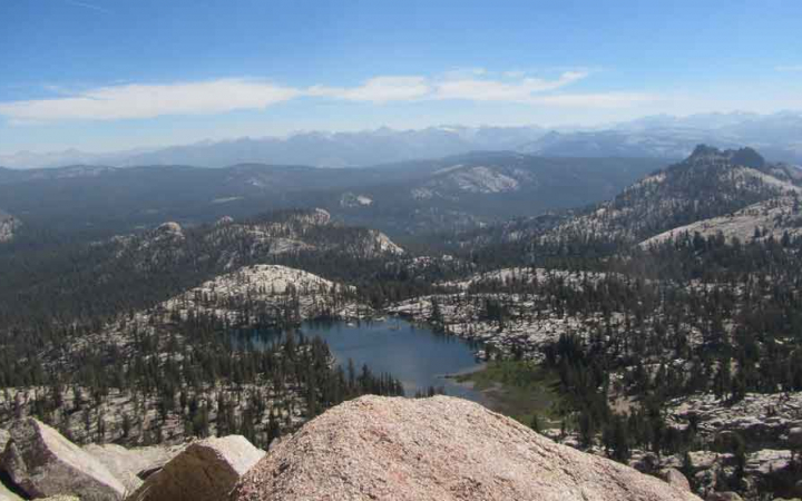 From a high point of view, an alpine lake rests amongst trees, rocks and mountains.